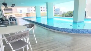 A pool area with a table and chairs, a view of the city, and a person standing by the pool. - F9 Brand NewSuite Delux Gym Pool Saune  (Santo Domingo)