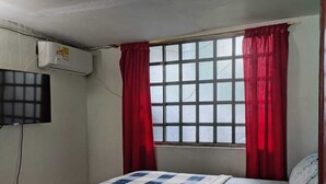 A bedroom with a bed, a window with red curtains, a mounted TV, and a small table with a remote control. - Brown 101 rest house (Villavicencio)