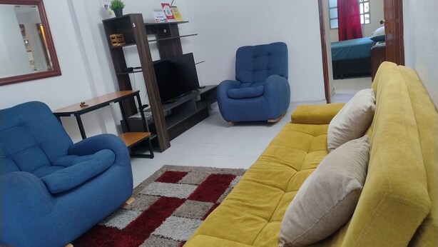 A living room with a sofa, a blue armchair, a TV on a stand, and a small table. - Brown 101 rest house (Villavicencio)