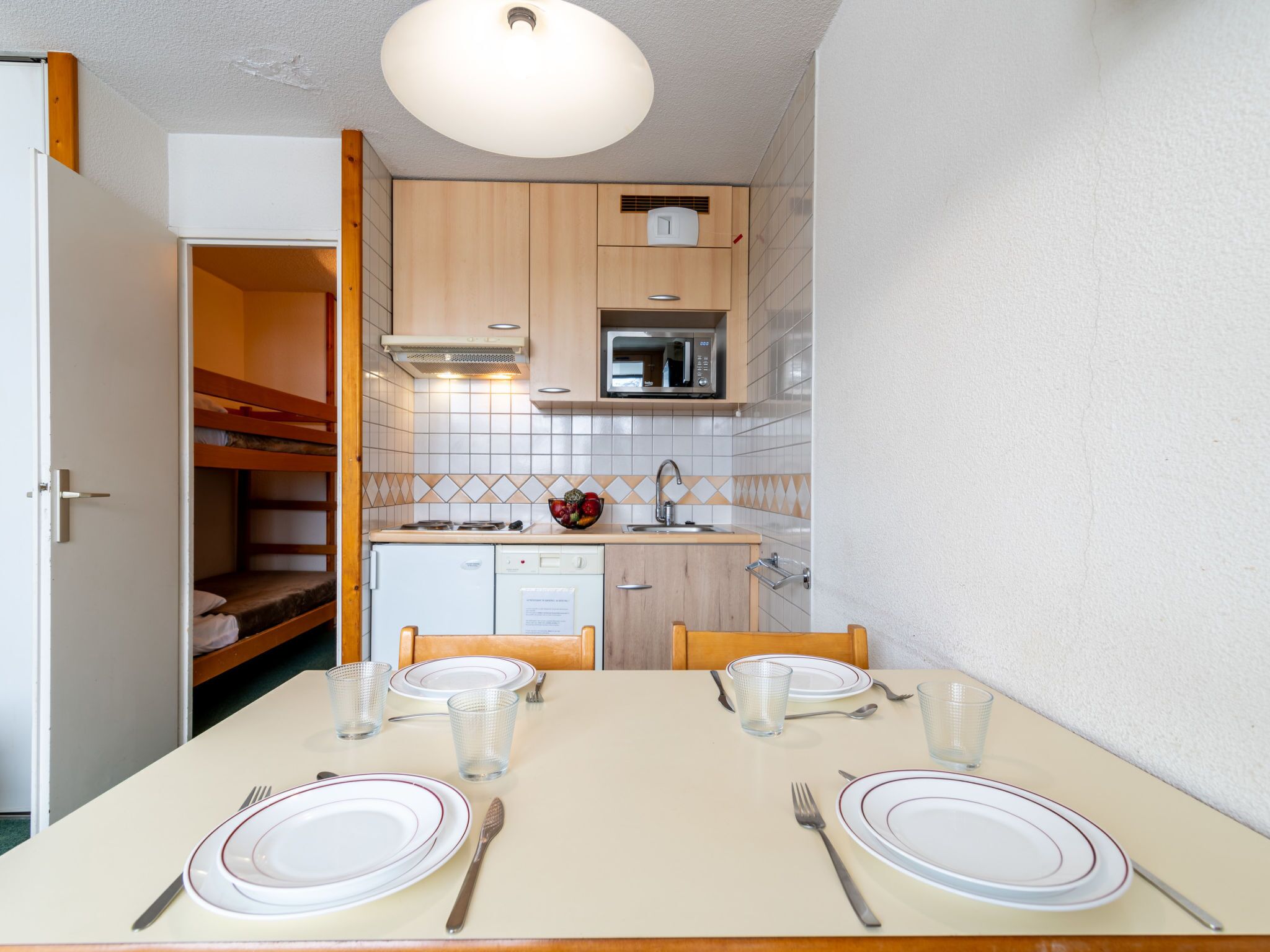 A compact kitchen with a dining table set for two, a microwave, and a small refrigerator.