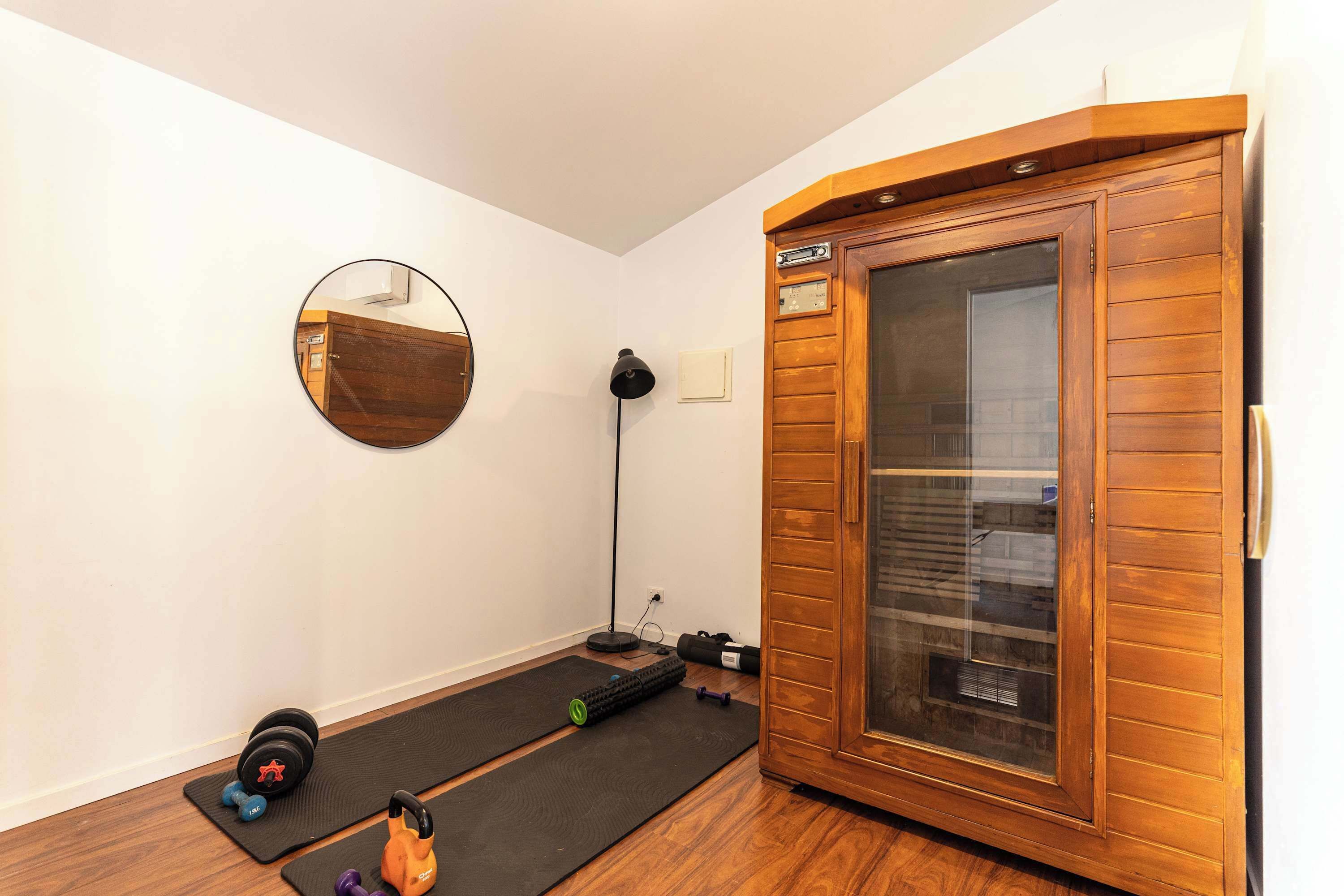 A room with a wooden cabinet, a mirror, a yoga mat, and exercise equipment.