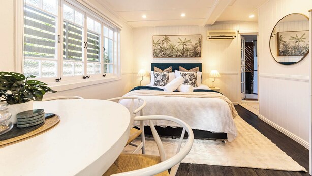 A bedroom with a bed, bedside lamps, a round mirror, and a window with shutters. - Urban Getaway Apartment Ipswich perfect for work (Newtown)