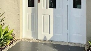A double white door with a glass panel, a small potted plant, and a tiled entrance area. - Urban Getaway Apartment Ipswich perfect for work (Newtown)