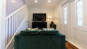 A living room with a green sofa, a fireplace, a television, and a staircase. - Urban Getaway Apartment Ipswich perfect for work (Newtown)