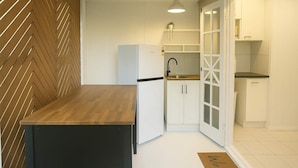 A compact kitchen with a wooden herringbone-patterned wall, a black countertop, white cabinets, and a black sink. - Urban Getaway Apartment Ipswich perfect for work (Newtown)