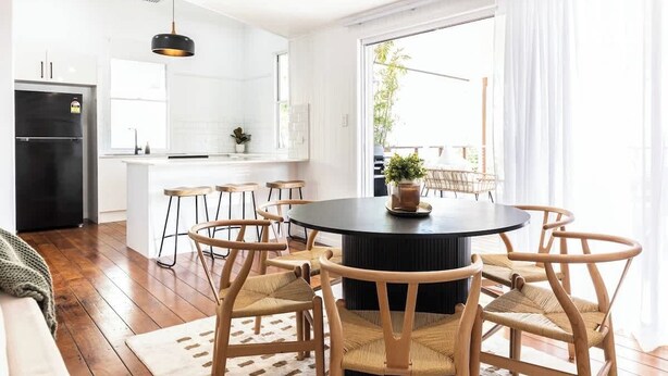 Een moderne keuken met witte kasten, een zwarte koelkast, en een eethoek met een ronde tafel en houten stoelen.