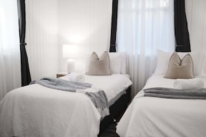 A hotel room with two beds, white bedding, a bedside lamp, and sheer curtains.