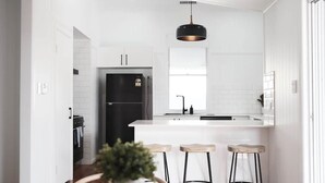 Een moderne keuken met witte kasten, een zwarte koelkast en een centraal keukenblok met krukken.