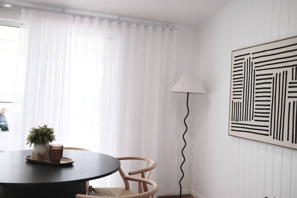 A room with a round table, two chairs, a potted plant, and a wall-mounted lamp.