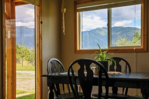 Un comedor con mesa y sillas, una ventana con vista a la montaña y una planta colgante.