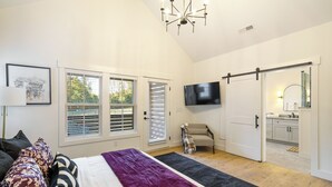 Un dormitorio con cama, televisor, sillón y puerta corrediza al baño.