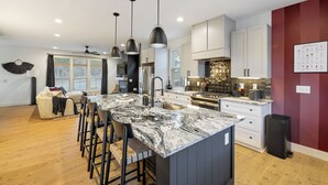 Una cocina moderna con una isla grande, taburetes de bar, iluminación colgante y una pared de acento roja.