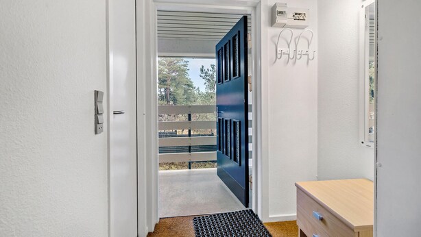 Un couloir avec une porte blanche, une porte bleue, un meuble en bois et une prise électrique sur le mur.