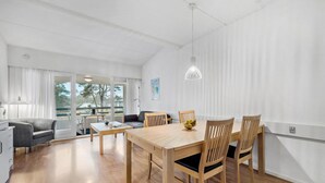Un espace de repas moderne avec une table et des chaises en bois, un canapé et une vue sur l’extérieur grâce à de grandes fenêtres.