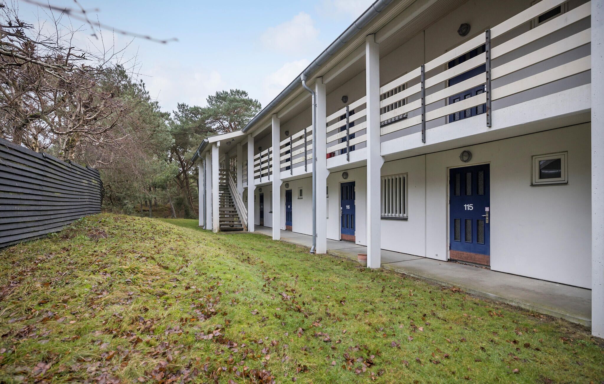 A row of white buildings with blue doors, numbered 115, and a staircase leading to the upper floor.