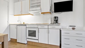 Une cuisine moderne avec des meubles blancs, un four encastré, une machine à café et un téléviseur à écran plat fixé au mur.