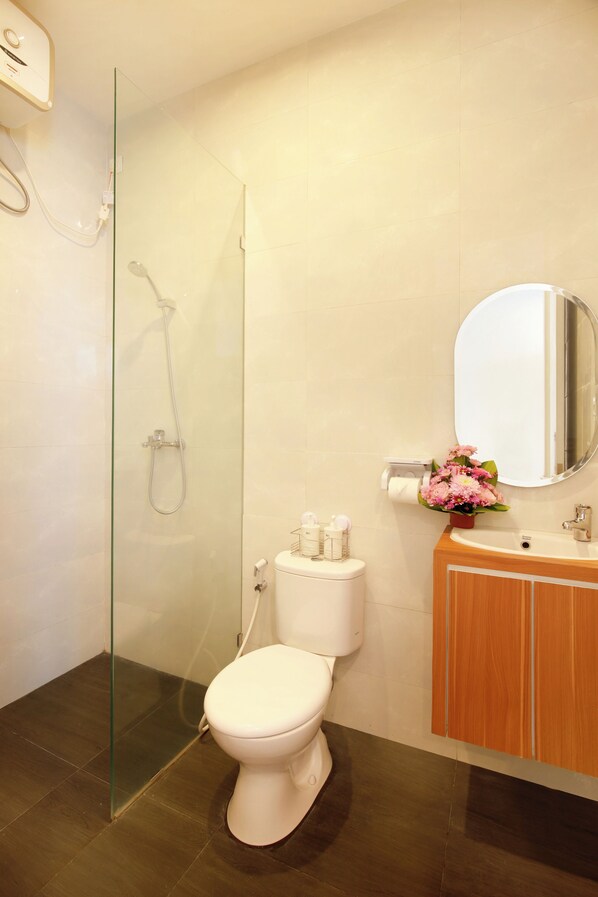 A bathroom with a glass-enclosed shower, a white toilet, a wooden vanity with a mirror, and a small flower arrangement.