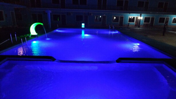 Una piscina con iluminación azul, rodeada por un edificio con múltiples ventanas.