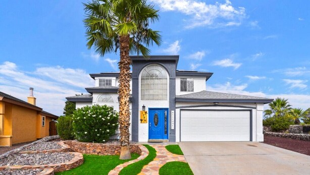 Een modern herenhuis met een blauwe deur, een garage en een verzorgd gazon met een pad van stenen.