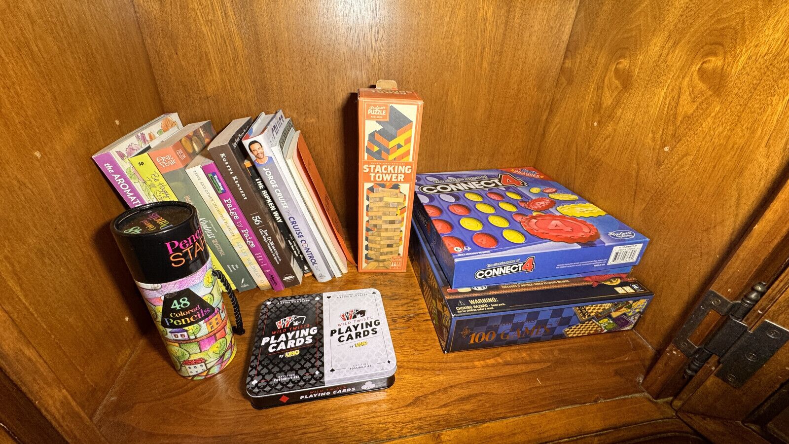 A wooden cabinet with various board games and a set of colored pencils.