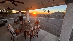 Een terras buiten met een ronde tafel en gestreepte stoelen met kussens, met uitzicht op een rotsachtig landschap en een zonsondergang.