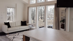 A modern living room with a white sofa, a coffee table, and large windows offering a view of the outdoors. - Farm Stay with Highland Cows (Mulberry)