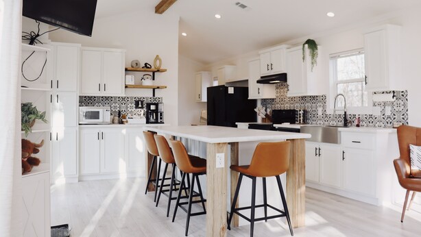 A modern kitchen with white cabinets, a central island with stools, a flat-screen TV mounted on the wall, and a hanging plant. - Farm Stay with Highland Cows (Mulberry)