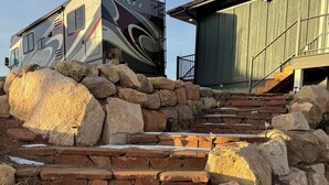 Un escalier en pierre mène à un bâtiment en bois, près duquel est garé un grand camping-car.