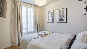 A hotel room with a bed, a window with curtains, and two wall-mounted artworks. - New Apartment Center of Paris/le Marais (Paris)