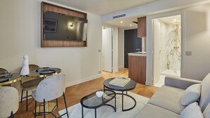 A modern living room with a sofa, a dining table with chairs, a TV mounted on the wall, and a kitchen area visible through an open door. - New Apartment Center of Paris/le Marais (Paris)