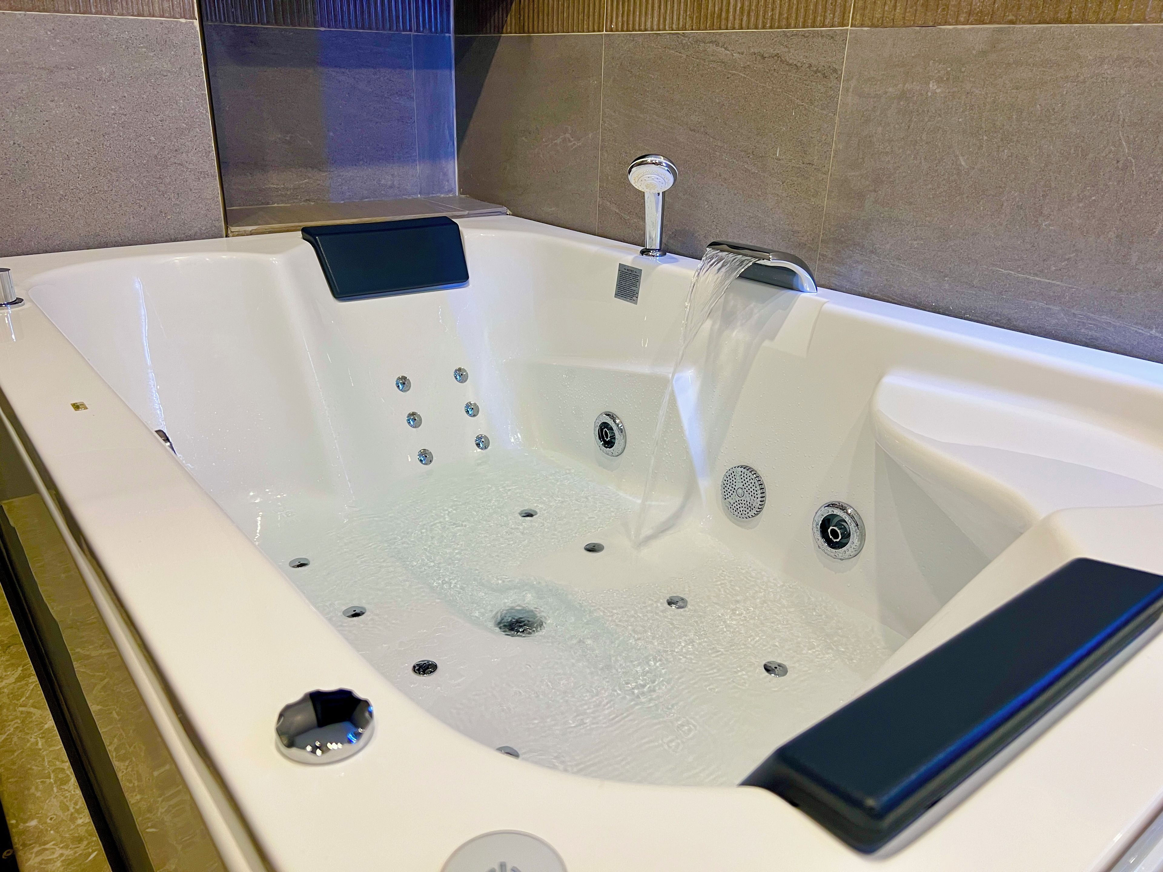 A white bathtub with multiple jets, a handheld showerhead, and a control panel.
