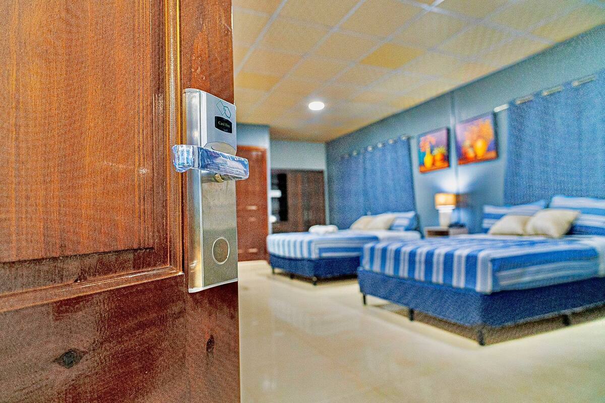 A hotel room with two beds, a wooden door, and a digital lock.