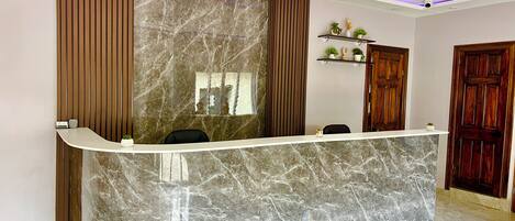 A reception desk with a marble top, flanked by wooden panels and a wall with a marble pattern.