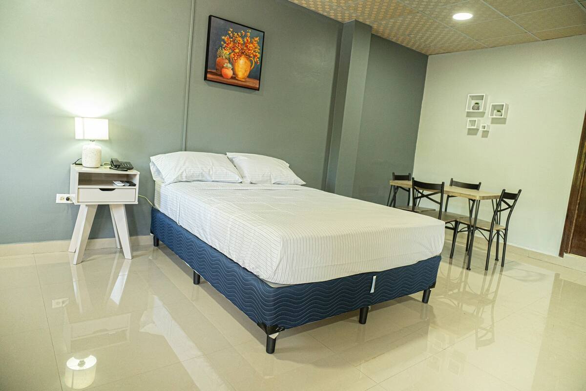 A bedroom with a bed, bedside table, lamp, and a painting on the wall.