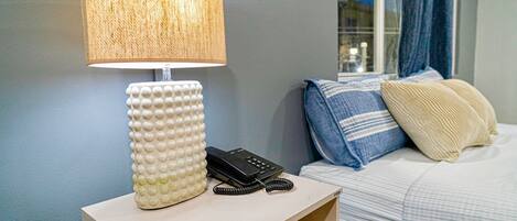 A hotel room with a bedside lamp, a phone, and a bed with pillows.