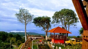 A wooden deck with a red-roofed pavilion, surrounded by lush greenery and a mountainous backdrop. - Hotel Five Stars sv (Berlin)