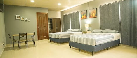 A hotel room with two beds, a dining table with chairs, a wardrobe, and a door.