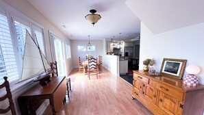 Un comedor amplio con una mesa y sillas de madera, una cocina al fondo y un ventanal con persianas.