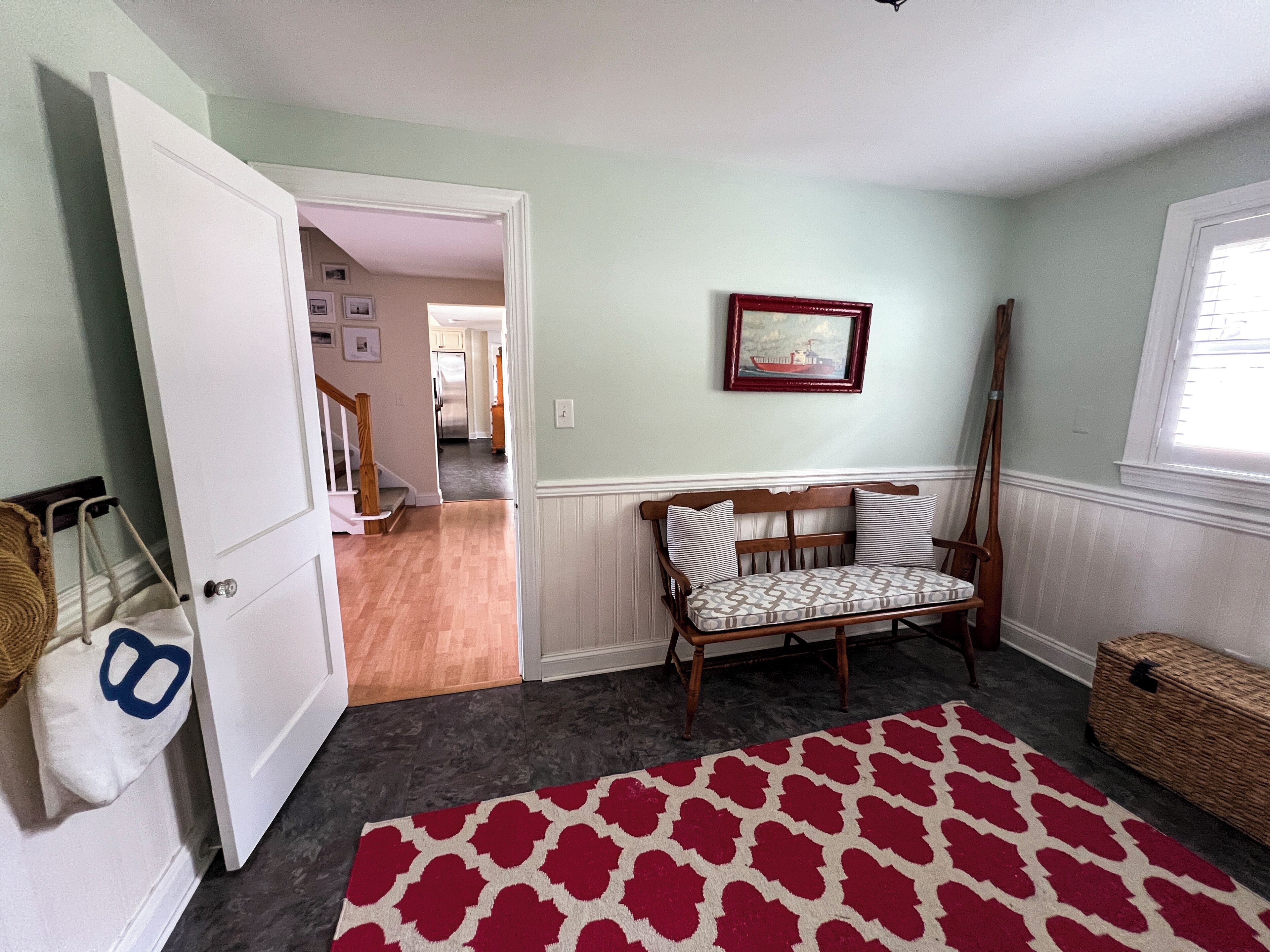 A room with a wooden bench, a red patterned rug, a wicker basket, and a door leading to another room.