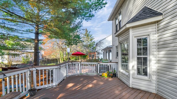 A wooden deck with a white railing, a red umbrella, and a house with white siding and a dark roof.