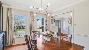 A dining area with a wooden table, chairs, a chandelier, and a window with curtains.