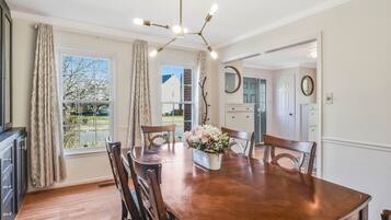 Un coin repas avec une table en bois, des chaises, un lustre et une fenêtre avec des rideaux.