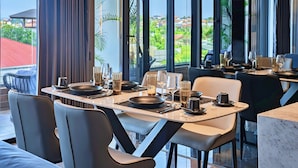 A modern dining area with a table set for four, featuring contemporary chairs and a view of a residential area through large windows. - The One Umalas (Kerobokan)