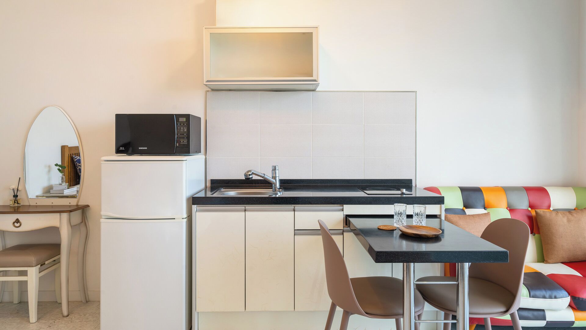 Eine kompakte Küchenzeile mit Mikrowelle, Spüle und einem kleinen Schrank. Ein Essbereich mit Tisch und Stühlen lädt zum Verweilen ein, und ein farbenfrohes Sofa bietet bequeme Sitzgelegenheiten.