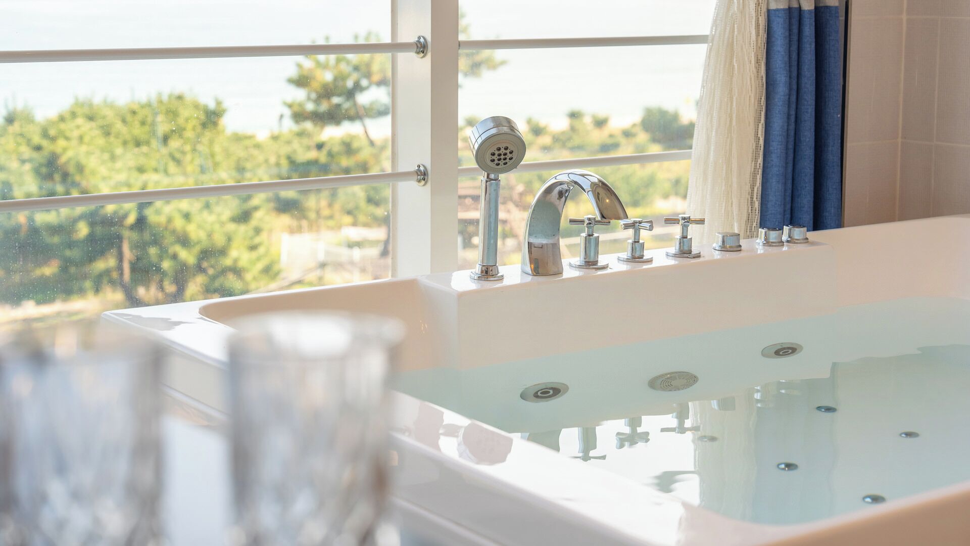 A bathroom with a bathtub, multiple faucets, and a view of greenery outside.