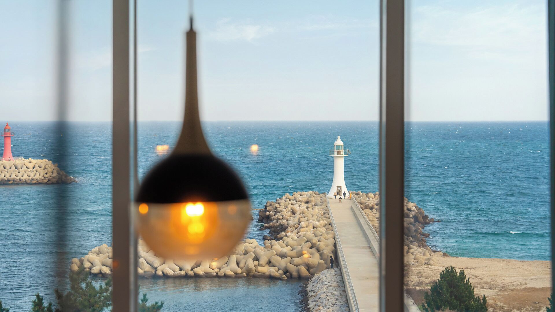 Panorama costiero con un faro, frangiflutti rocciosi e mare calmo.