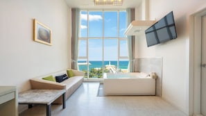 A modern hotel room with a large window, a sofa, a small table, a bathtub, and a flat-screen TV. - Gangneung Meerbrick Spa Pension (Gangneung)
