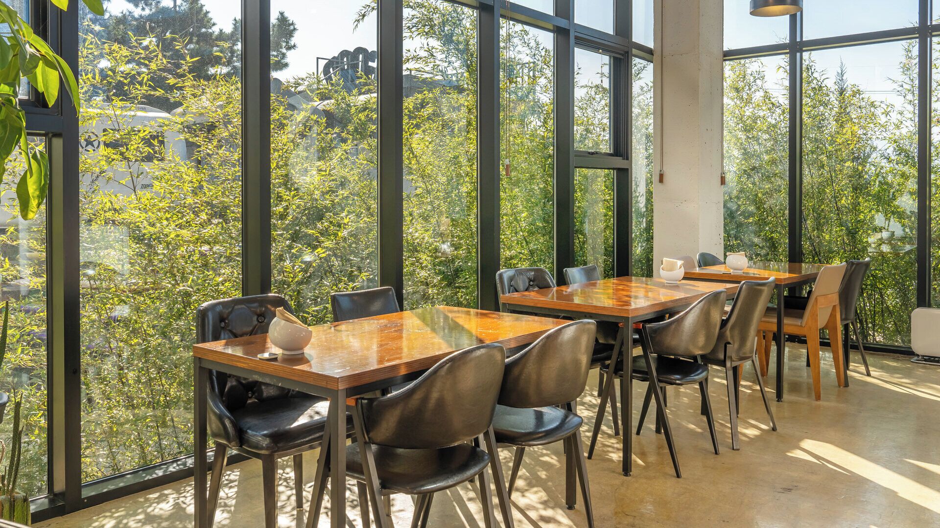 A dining area with large windows, wooden tables, and black chairs.