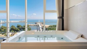 Un bagno moderno con una vasca da bagno ampia, vista sul mare e un molo in pietra.