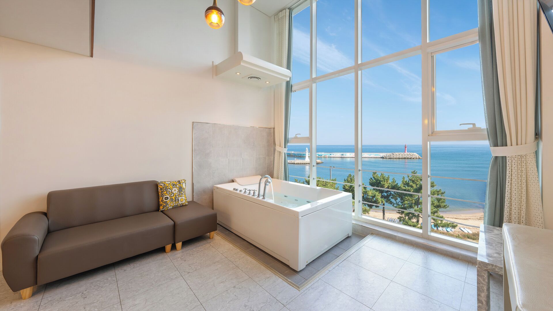Een moderne badkamer met een badkuip, een bank en een groot raam met uitzicht op zee.
